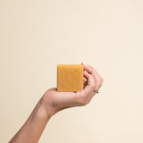 Hand holding Paca Botanica Marigold Brightening Soap Bar with turmeric and calendula, showcasing its rich golden hue.