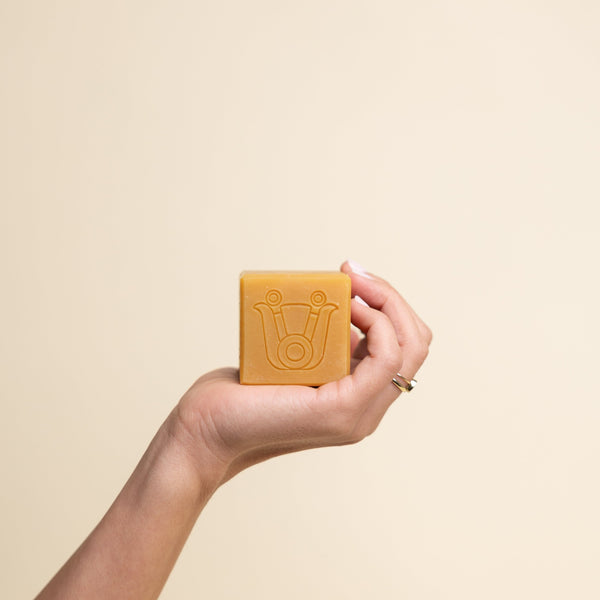 Hand holding Paca Botanica Marigold Brightening Soap Bar with turmeric and calendula, showcasing its rich golden hue.