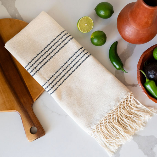 Cotton Woven Kitchen Hand Towel in natural with slate grey stripes and 100% cotton fringe laying flat on counter with limes, jalapenos, tomatoes and avocados in the background