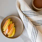Cotton Woven Kitchen Hand Towel in natural with slate grey stripes and 100% cotton fringe laying flat on marble counter with mango on a plate