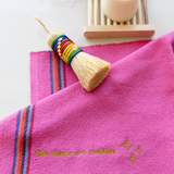 Fuchsia pink cotton cleaning cloth known as Jerga in Mexico with gold embroidery. Three gold stars embroidered on the cloth and a phrase reading "Solo limpio con cumbias". An agave escobeta layin on the top left hand corner.