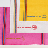 Three recycled cotton cleaning cloths known as "jerga" in Mexico laying on top of eachother: Yellow with blue embroidery, White with red embroidery, fushia pink with gold embroidery