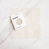 Ayate washcloth (a woven agave fiber mesh wash cloth) with Volvere branded box on a marble surface