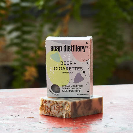 Soap Distillery Beer and Cigarettes Bar Soap with label that says smells like dried tobacco leaves, lavender and hops. Greenery in the background