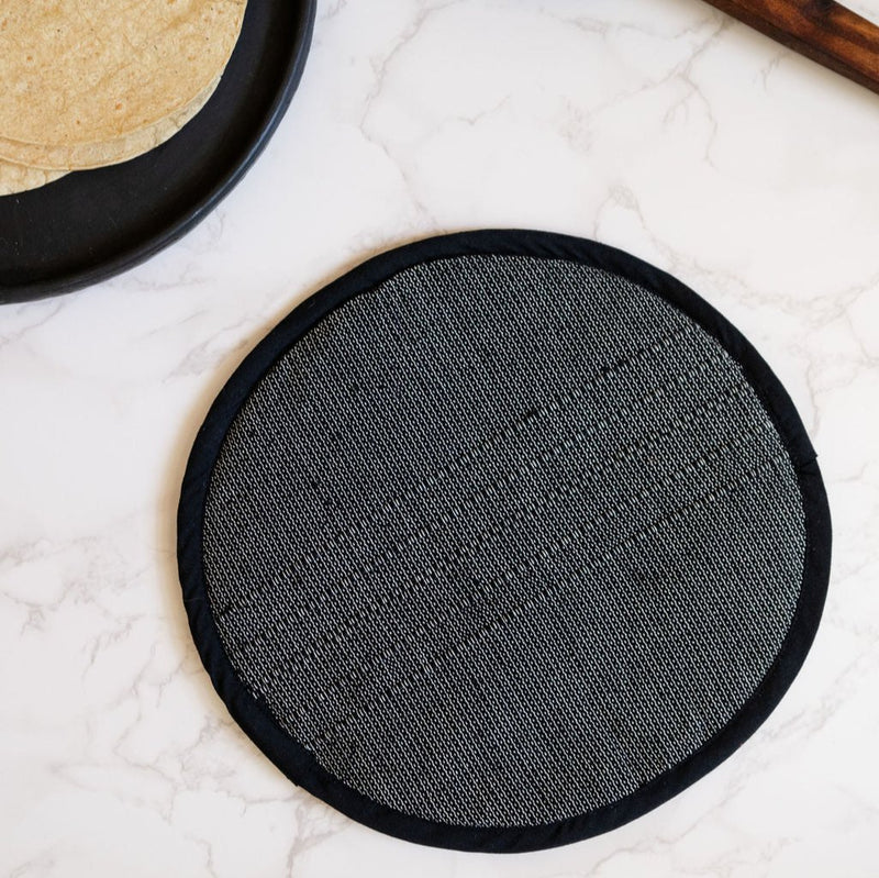 A Black Handwoven Cotton Tortilla Warmer sits elegantly on a table, showcasing its natural, dark tones and intricate handwoven texture. Made from 100% cotton, this eco-friendly warmer adds a rustic, artisan touch to any meal while keeping tortillas warm and fresh.