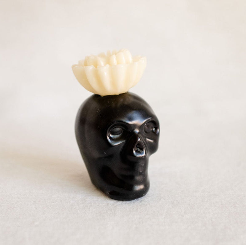 Black Obsidian Skull Candle with a white flower top, made from 100% beeswax, perfect for home decor or altars, offering a unique blend of bold design and natural elements.