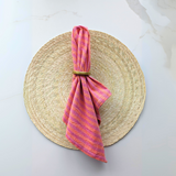 Handwoven cotton napkin in Orange and Pink stripes on a round palm placemat. Ethically made.