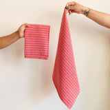 Handwoven cotton napkin in Orange and Pink stripes held by a hand against a wall. Ethically made.