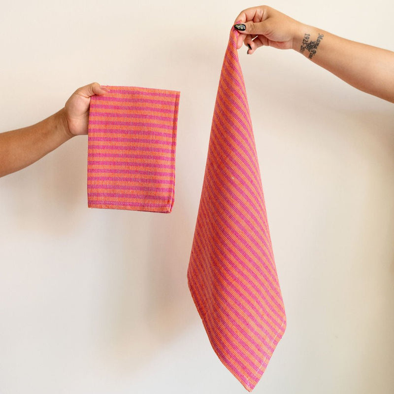 Handwoven cotton napkin in Orange and Pink stripes held by a hand against a wall. Ethically made.