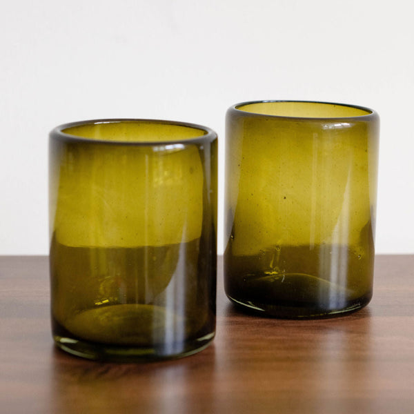 Two Mexican recycled olive green glass tumblers on a wooden surface with a white background
