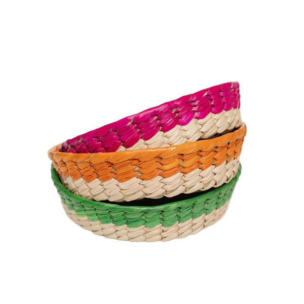Mexican woven palm baskets with different color rims: pink (Rosa Mexicano), Orange (Apricot), and green (Emerald Green) stacked on white background