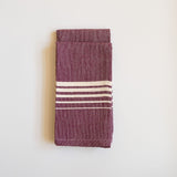 Set of two Purple Jacaranda Casa Oaxaca Cotton Napkins feature a rich, purple hue adorned with five evenly spaced white lines, creating a striking contrast. Handwoven from 100% Mexican cotton, this eco-friendly napkin adds a vibrant, artisanal touch to any sustainable table setting, perfect for eco-conscious dining.