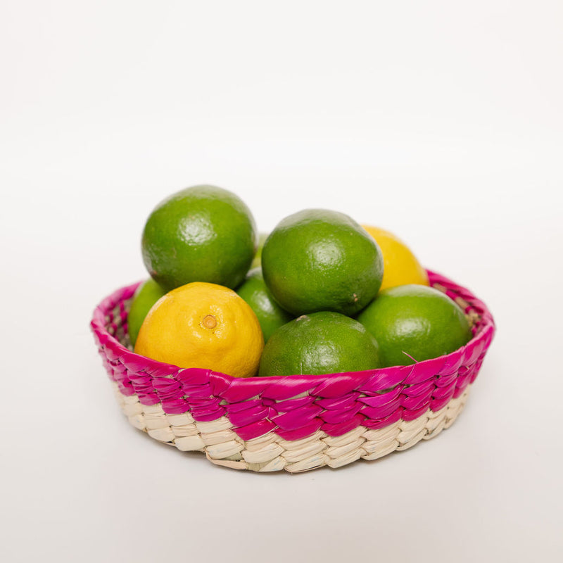 Mexican Palm basket with a pink (Rosa Mexicano) color rim and natural bottom filled with lemon and limes