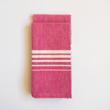 A vibrant Set of Two Rosa Mexicano (Pink) Casa Oaxaca Woven Cotton Napkins, showcasing artisanal craftsmanship from Oaxaca, Mexico, with a soft, durable texture perfect for adding a pop of color to any table setting. This eco-friendly, 100% cotton napkin is handwoven, blending sustainable design with traditional Mexican culture.