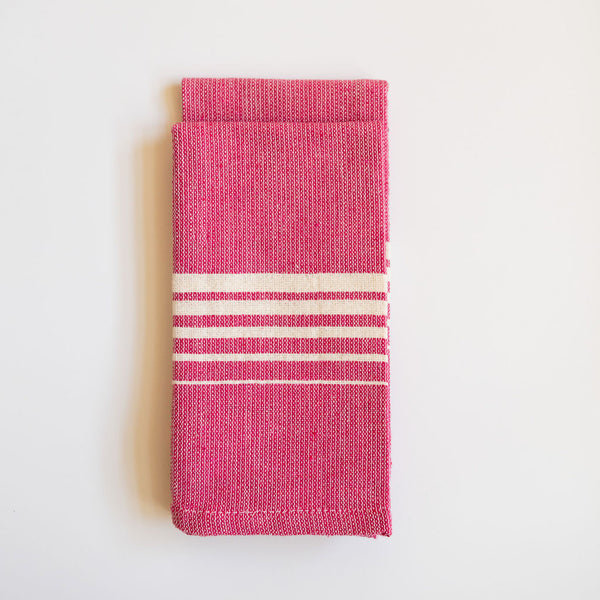 A vibrant Set of Two Rosa Mexicano (Pink) Casa Oaxaca Woven Cotton Napkins, showcasing artisanal craftsmanship from Oaxaca, Mexico, with a soft, durable texture perfect for adding a pop of color to any table setting. This eco-friendly, 100% cotton napkin is handwoven, blending sustainable design with traditional Mexican culture.