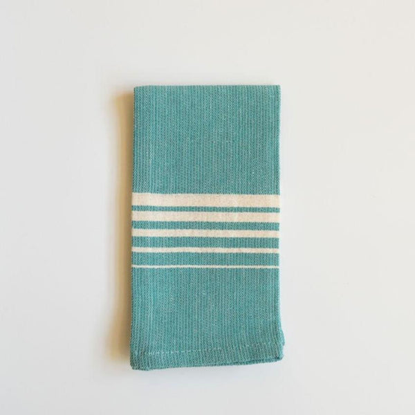 A vibrant Teal Casa Oaxaca Woven Cotton Napkin, crafted from 100% Mexican cotton, adds a pop of color to any table setting with its artisanal design and sustainable, eco-friendly material. Perfect for elevating your dining experience, this napkin is handwoven in Oaxaca and designed to complement a modern, conscious lifestyle.