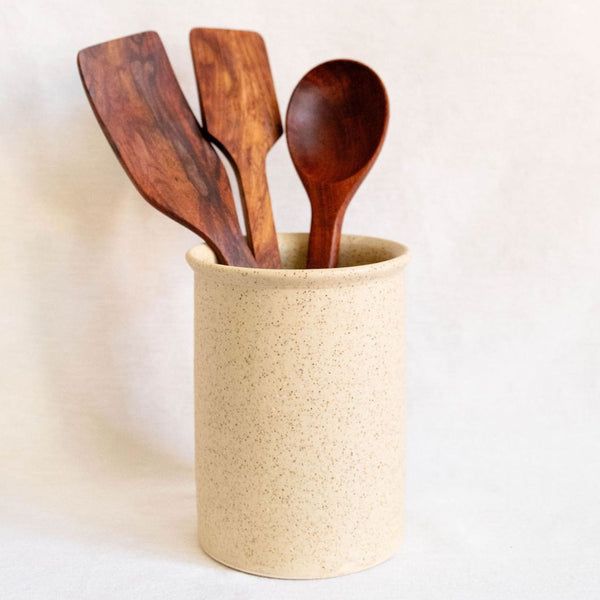 Speckled vanilla ceramic utensil crock holding three handcrafted wooden kitchen utensils