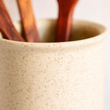 Speckled vanilla ceramic utensil crock holding three handcrafted wooden kitchen utensils