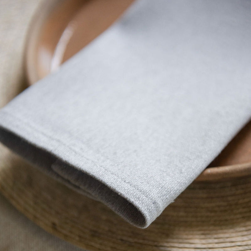 Light grey cotton dinner napkin on a plate and palm placemat