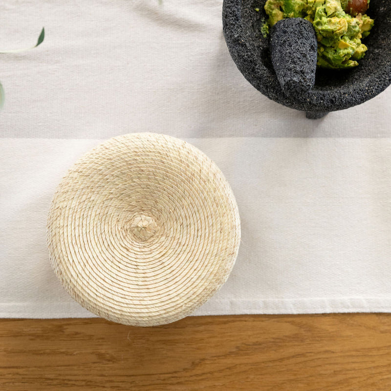 Top view of handwoven palm tortilla warming basket on a dinner table with molcajete and guacamole