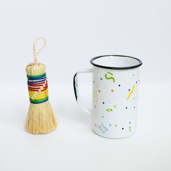 Agave Cleaning Brush (Escobeta) with rainbow string standing next to a tall enamel mexican peltre cup with confetti dots