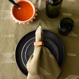 Table setting with black plates, olive green cotton napkin, and an olive green table runner with geometric shapes