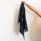 Handwoven Cotton Black hand and dish towel with geometric patterns and fringes held by a hand against a light background