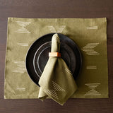 Olive green handwoven geometric placemat with black plate and folded olive green cloth napkin