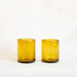 Two amber gold glass tumblers on a white background