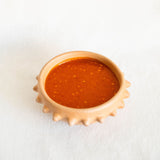 Terracotta ceramic clay (barro) bowl with pointed spike rim filled with red salsa on a white background