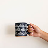Hand holding Tzintzuntzan handmade ceramic mug with mountain pattern, burnished clay pottery from Michoacán Mexico, natural matte finish coffee cup with hand holding mug