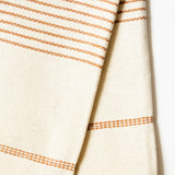 A close-up of a woven cotton hand towel in a warm cream color with thin horizontal terracotta dotted stripes, shown against a plain white background.