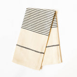 A folded cream-colored cotton kitchen towel with black woven stripes, shown on a clean white background.