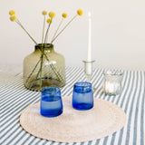 Handblown Recycled Glass Candle Holders, flower vase, and cups paired with cotton stripe tablecloth and palm placemat all made in Mexcio.