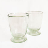 Two small clear glass tumblers with footed bases, photographed on a plain white background.