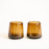 Two chocolate brown glass tumblers with a tapered shape, standing side-by-side on a plain white background.