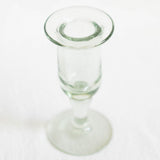 A clear glass candle holder with a flared rim and a short stem, photographed on a plain white background.