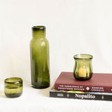 Three olive green glass candle holders of different sizes displayed on and beside two books on a white background.