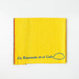 A close up of a yellow recycled cotton cleaning cloth known as Jerga with blue embroidery reading "Un Rinconcito del cielo" and a blue cloud