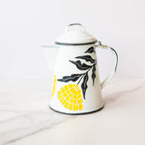 White enamel (peltre) kettle with vibrant yellow marigold designs and black leaf accents, set against a marble background.