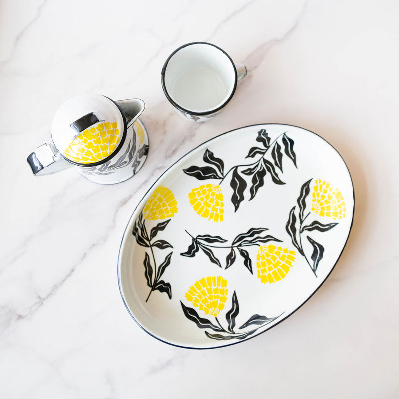 White enamel (Peltre) Cup, kettle, and tray with vibrant yellow marigold (cempasúchil) designs and black leaf accents, set against a marble background.