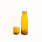 An amber-colored glass bottle with matching lid/cup on a white background
