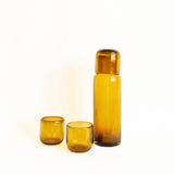 Set of two amber glass tumblers next to a matching glass bedside carafe on a white background