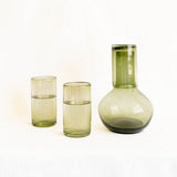 Set of green Mexican glassware including a round carafe and two olive green glasses on a white background