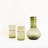 Set of green handblown glassware including two highball tumblers and a round carafe with lid on a white background