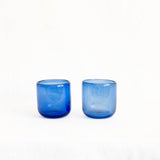 Two small cobalt blue handblown glass cups or candle holders standing side by side on a plain white background.