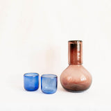 Two cobalt blue Mexican glass tumblers and an amethyst glass carafe on a white background