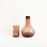 A round glass carafe and matching lid that serves as a cup both in amethyst against white background