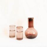 two amethyst glass cups with a matching round glass carafe 