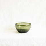 A Mexican handblown glass olive green glass bowl with a darker base, photographed against a plain white fabric background.
